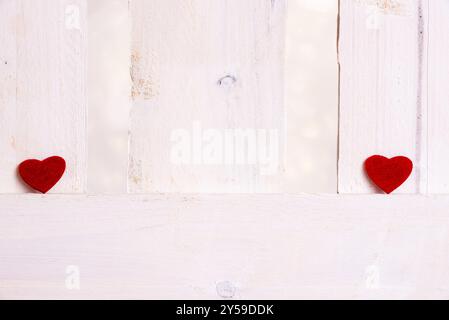 Cute little red hearts, displayed one on the left and one on the right of a white wooden fence. A concept of love, breakup, romance, valentine day Stock Photo