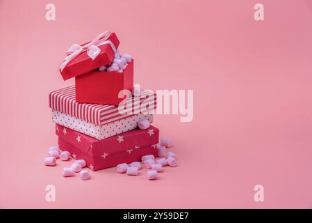 Christmas gifting theme image with a stack of gifts wrapped in different red designs, full of pink tiny marshmallows, on a pink paper background Stock Photo