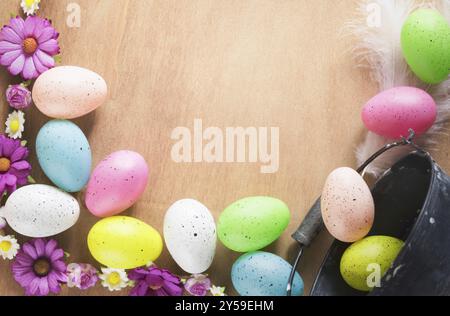 Easter frame design with a bunch of multicolored painted eggs, colorful spring flowers and feathers, displayed on a table with space for text Stock Photo