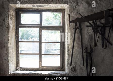 Aged window and blacksmith tools hanging on an old wall, in the interior of a German house Stock Photo
