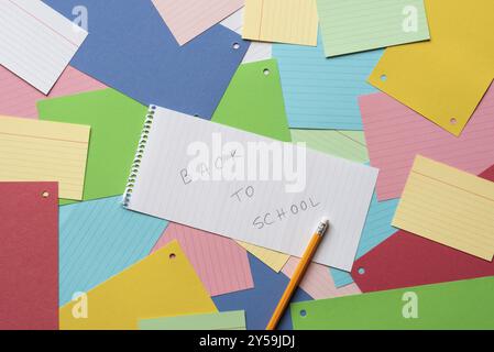 Notebook sheet with the message back to school against a background of colorful paper notes Stock Photo