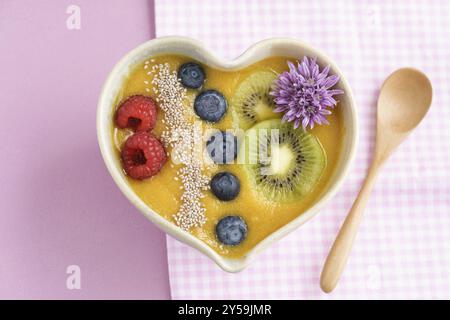 Peach smoothie bowl with blueberries, kiwi, white chia seeds and raspberries in a heart shaped bowl Stock Photo