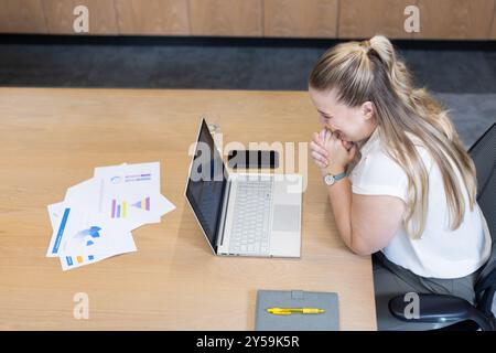 At office, woman analyzing charts on laptop at desk with documents Stock Photo