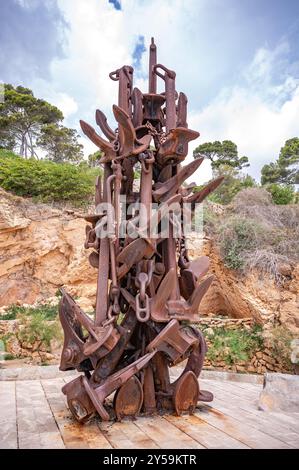 A towering, rusty sculpture majorca of intertwined anchors stands against a backdrop of dramatic cliffs and a Mediterranean sky, symbolizing the raw p Stock Photo