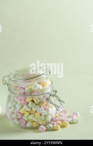 Fluffy and colorful marshmallow overflow from a big glass jar on the green vibrant background Stock Photo