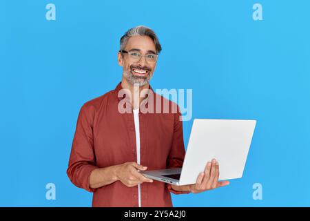 Smiling mature professional man holding laptop isolated on blue background. Stock Photo