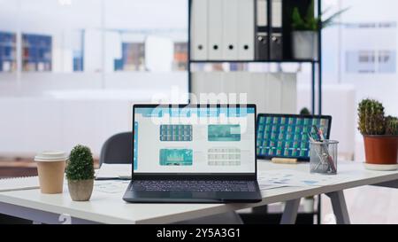 Financial analyst workspace featuring laptop and tablet displaying stock market data and statistics. Devices on desk in office next to paperwork with forex trading economic analytics figures Stock Photo