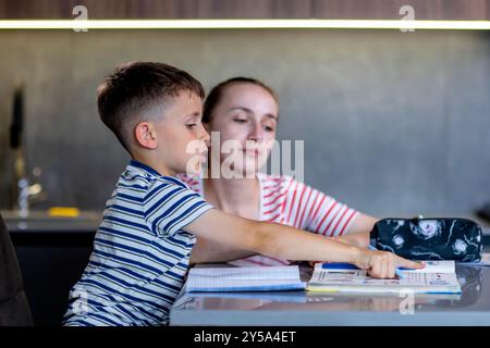 Mother helping her son doing homework in kitchen. Stock Photo