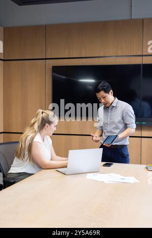 At office, Business meeting, asian man presenting data on tablet to woman using laptop Stock Photo