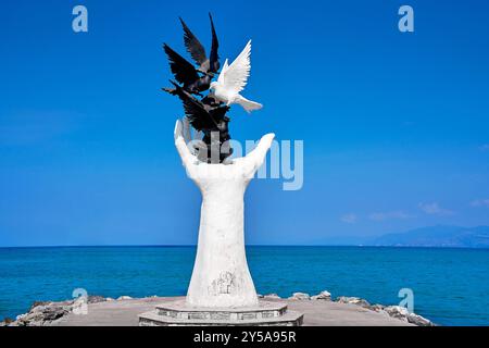 Kusadasi, Turkey - 1 September 2024: The Hand of Peace sculpture in Kusadasi stands by the sea and shows a white hand releasing several doves, symbolizing peace and freedom *** Die Hand of Peace-Skulptur in Kusadasi steht am Meer und zeigt eine weiße Hand, die mehrere Tauben freilässt, symbolisierend Frieden und Freiheit Stock Photo