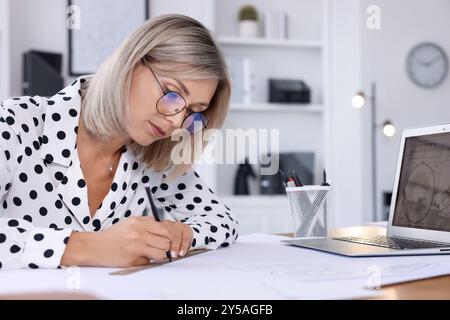 Architect making engineering drawing at table in office Stock Photo