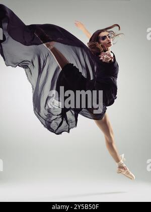 Ballet, woman and portrait in black dress for jump, dancing and performance in studio. Ballerina, movement and makeup on gray background for talent Stock Photo