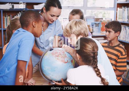 Children, teacher and map with globe in library for geography education, planet learning and and science. Students, woman and global teaching with Stock Photo