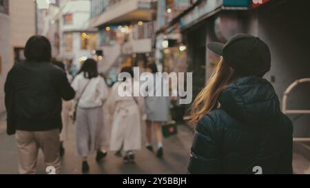 Stylish blonde woman leads her friends through tokyo's bustling streets, exuding a modern vibe in a black cap and jacket Stock Photo