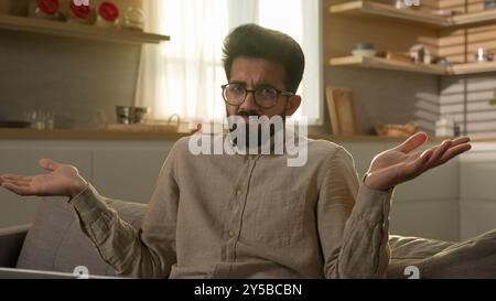 Indian Arabian muslim man in kitchen freelancer businessman working laptop from home puzzled shrugging shoulders don't know male customer confused Stock Photo