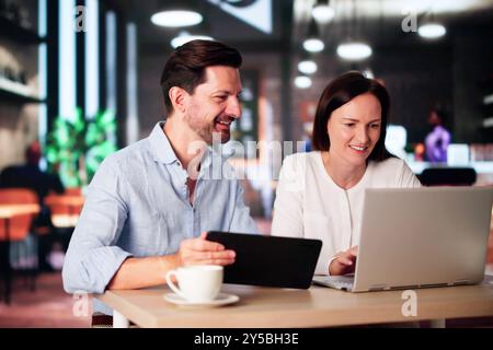 Coworkers Using Technology Lifestyle. Man And Woman Drinking Coffee In Cafe Stock Photo