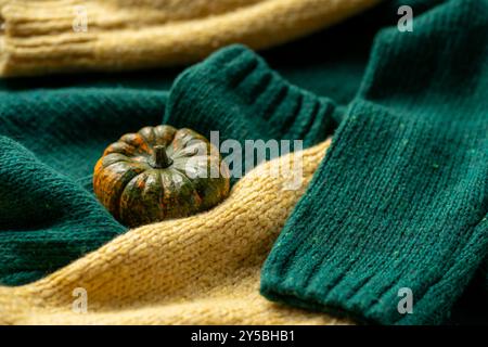 Orange pumpkin near a stack of knitted sweaters on a knitted blanket. Stock Photo