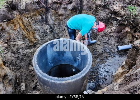 Using hammer drill with chisel, worker made hole in concrete ring of septic tank. Stock Photo