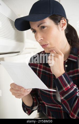 female contractor reading instructions for programming air conditioning unit Stock Photo