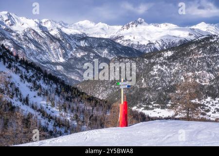 View on sign showing directions for blue and green ski slopes, in background valley and snowy mountains on border of France and Italy in Cottian Alps Stock Photo