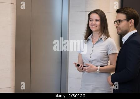 Confident coworkers standing in office hall, waiting for elevator Stock Photo