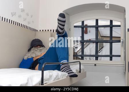 A man with a beard is sleep on a bunk bed in a prison cell Stock Photo