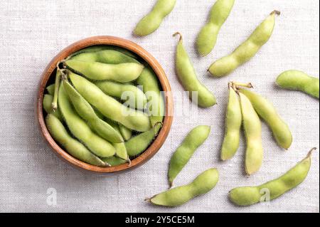 Fresh edamame, green soybeans in the pod, in a wooden bowl, on linen. Raw immature soybeans, Glycine max, used boiled or steamed and salted. Stock Photo