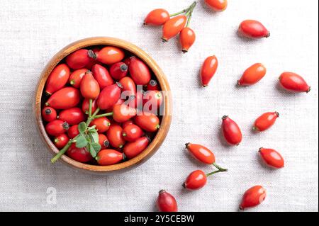 Fresh rose hips in a wooden bowl on linen. Also rose haw or rose hep, intense red ripe fruits, used for herbal teas, jam and can be eaten raw. Stock Photo