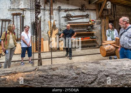 A museum guide explains century-old saws and tools to four visitors at the Amanda mill in Kappeln. Built in 1888 in the Dutch style, the mill is the only surviving combined grinding and sawmill in Schleswig-Holstein and was operated as a grain mill until 1964. Schleswiger Straße, Schleswig-Holstein, Germany. Stock Photo