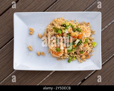 A vibrant shrimp fried rice garnished with crunchy peanuts, fresh scallions, and toasted sesame seeds, beautifully displayed on a white plate against Stock Photo