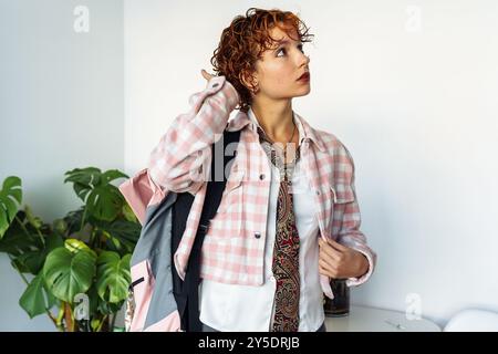attractive extravagantly dressed young woman, student, schoolgirl with red curly hair with backpack in home interior Stock Photo