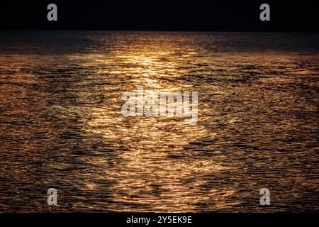 Sunset under a dark sky reflected in the sea at Bonniebrook Beach in Gibsons, BC, Canada. Stock Photo