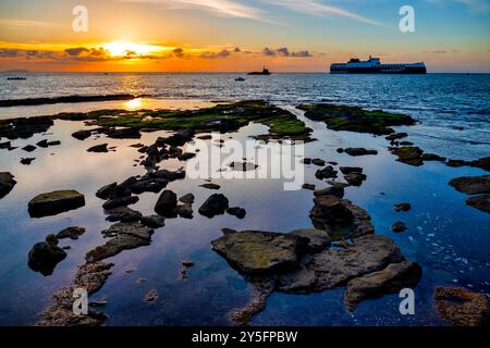 Sunset over the rocky coast of Livorno, Italy, near Terrazza Mascagni, with reflections in the tide pools and a distant ship. Stock Photo