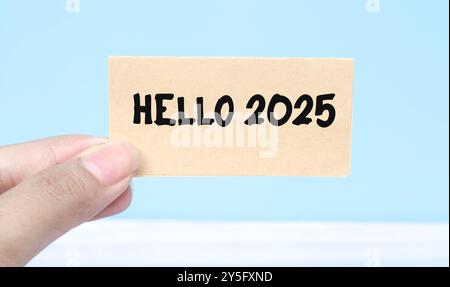 Hand holding note Hello 2025 isolated blue background. New year concept with typographic 2025. Motivational words to welcome the new year 2025 Stock Photo