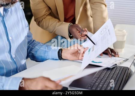 Diverse team analyzing business reports in modern office with documents, coffee cup, and laptop present. Close collaboration and teamwork evident during work process Stock Photo