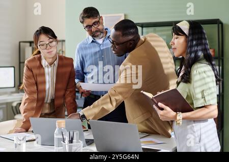 Colleagues sharing ideas and discussing plans in modern office room. Diverse team engaging in collaborative work environment focusing on team project Stock Photo