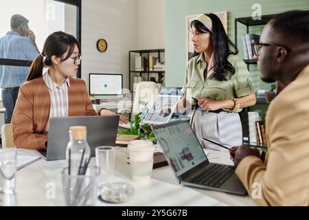 Team members collaborating on project details in office setting, with laptops and visual aids enhancing presentation impact Stock Photo