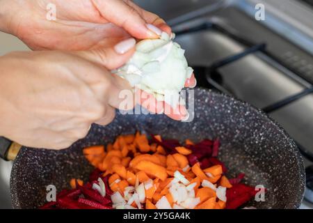 Shot of the freshly cut beetroots, onions and carrots stewed on the frying pan Stock Photo