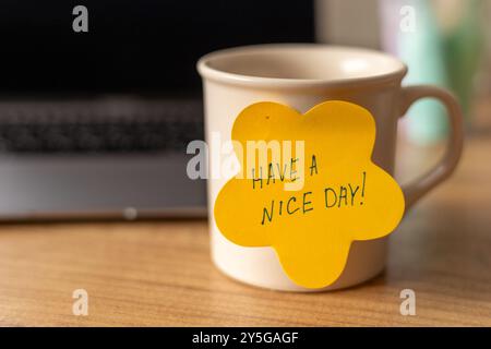 A cheerful reminder on a mug beside a laptop at a cozy workspace in the morning Stock Photo