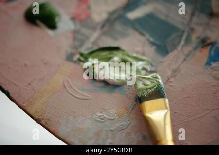 Artistic close-up showcasing paintbrush resting on paint palette with various paint blobs. Visible textures and colors emphasize process of creating an artwork Stock Photo