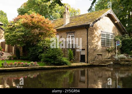 Canal side cottage with reflections of autumn trees including acer in canal. Estate agents board outside the house. Bollington, Cheshire, UK. Stock Photo