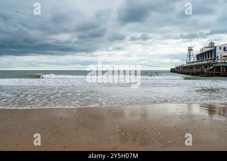 East Cliff Beach, Bournemouth, UK - March 26th 2023: The wet sand on the beach next to Bournemouth Pier with a surfer lineup. Stock Photo