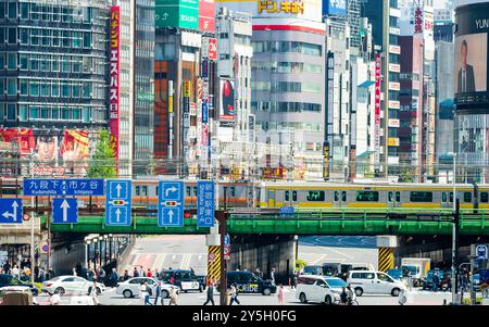 Famous Shinjuku viewpoint. Railway bridge over Ome-Kaido Avenue with a compressed perspective view of the Yunika Building and others. Train on bridge. Stock Photo