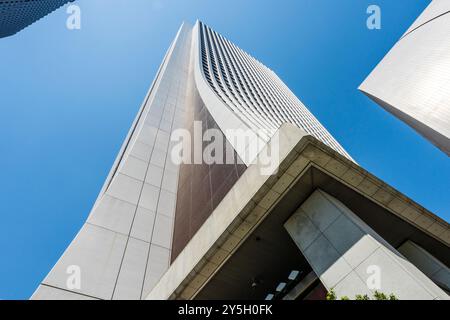 View up the SOMPO building in Shinjuku, Corner angle of the concrete tower with its curving facade as it towers up into the blue sky. Stock Photo