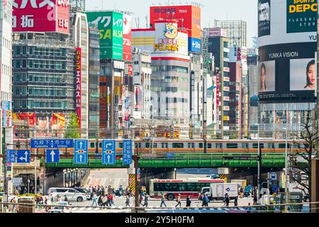 Famous Shinjuku viewpoint. Railway bridge over Ome-Kaido Avenue with a compressed perspective view of the Yunika Building and others. Train on bridge. Stock Photo