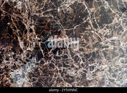 Close-up of a polished dark brown marble surface with intricate white veins and natural patterns, showcasing its rich texture and luxurious design. Stock Photo