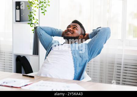 Dreamy black employee resting at workplace with hands behind head Stock Photo