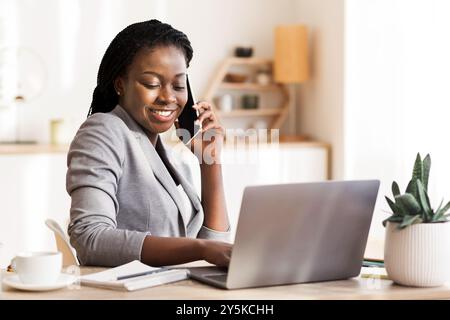Afro Businesswoman Talking On Cellphone And Using Laptop In Office Stock Photo