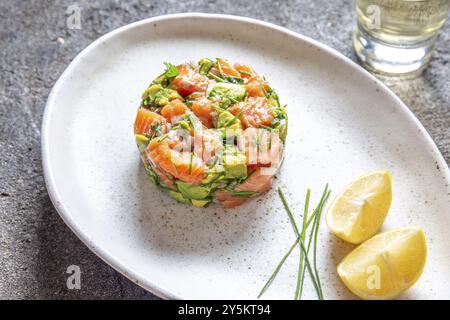 PERUVIAN FOOD. Salmon ceviche with avocado, spring onion and lemon on white plate served with white wine Stock Photo