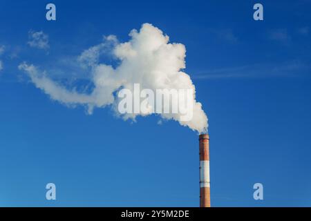 Large smokestack emits a billowing cloud of white smoke against a vibrant blue sky Stock Photo